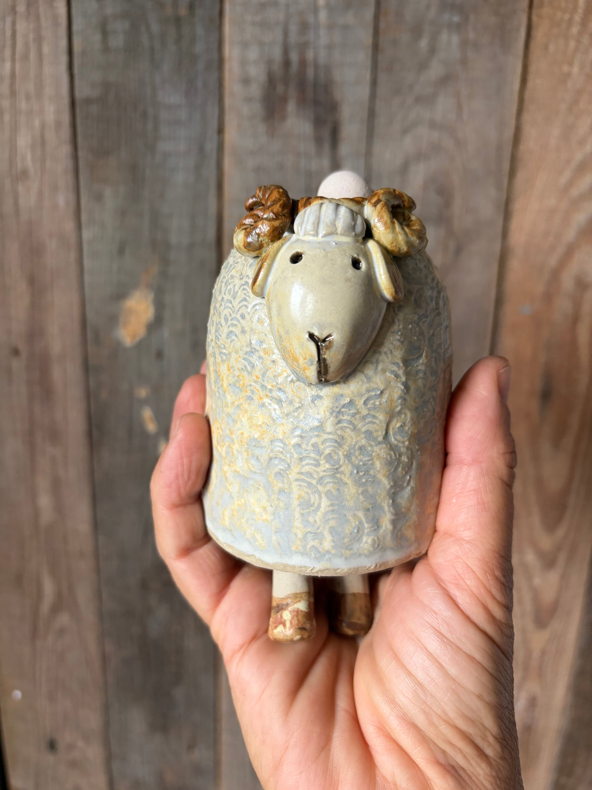 una mano regge una tintinnante campanella in gres a forma di montone
