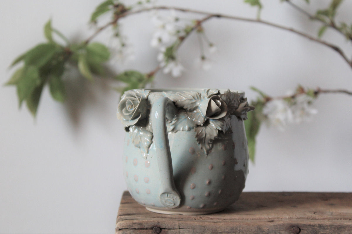 Tazza Alice in gres azzurro con rose bianche e puntini rosa in rilievo, fatta a mano al tornio